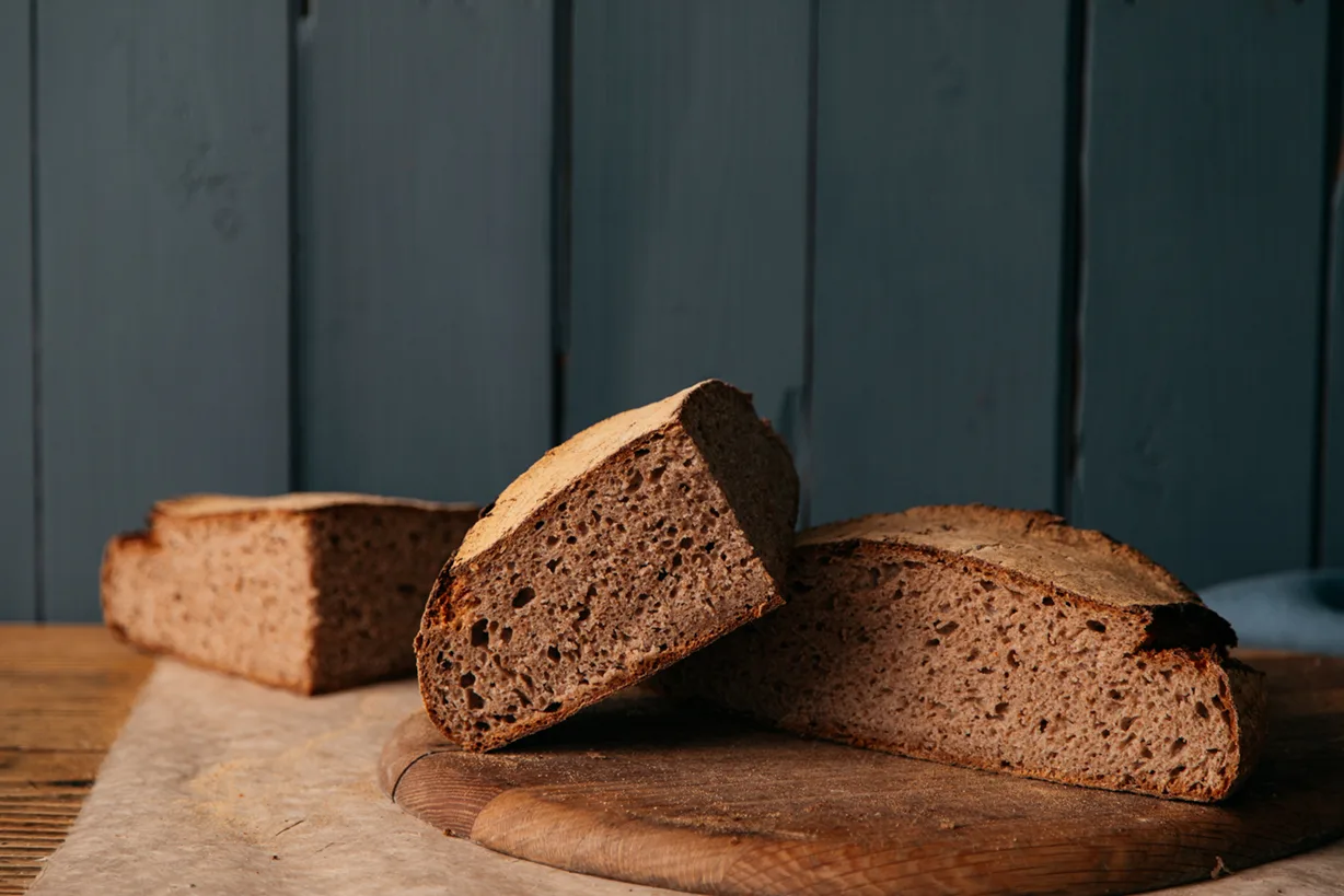 A cut loaf of Lovingly Artisan Wholemeal Barber Wheat Sourdough on a wooden board, showing a dense brown crumb